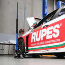 This is an image of a Kincrome 1-ton aluminum racing jack lifting a red Rupes racing car in a workshop, featured by Kennedys Welding Supplies in Derwent Park, TAS.