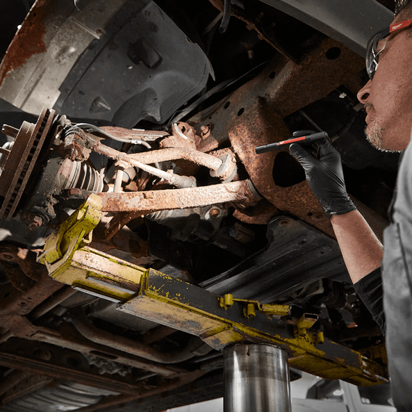 This is an image of a technician inspecting rusted car parts on a hydraulic lift at Kennedys Welding Supplies in Derwent Park, TAS, offering welding and power tool repairs.