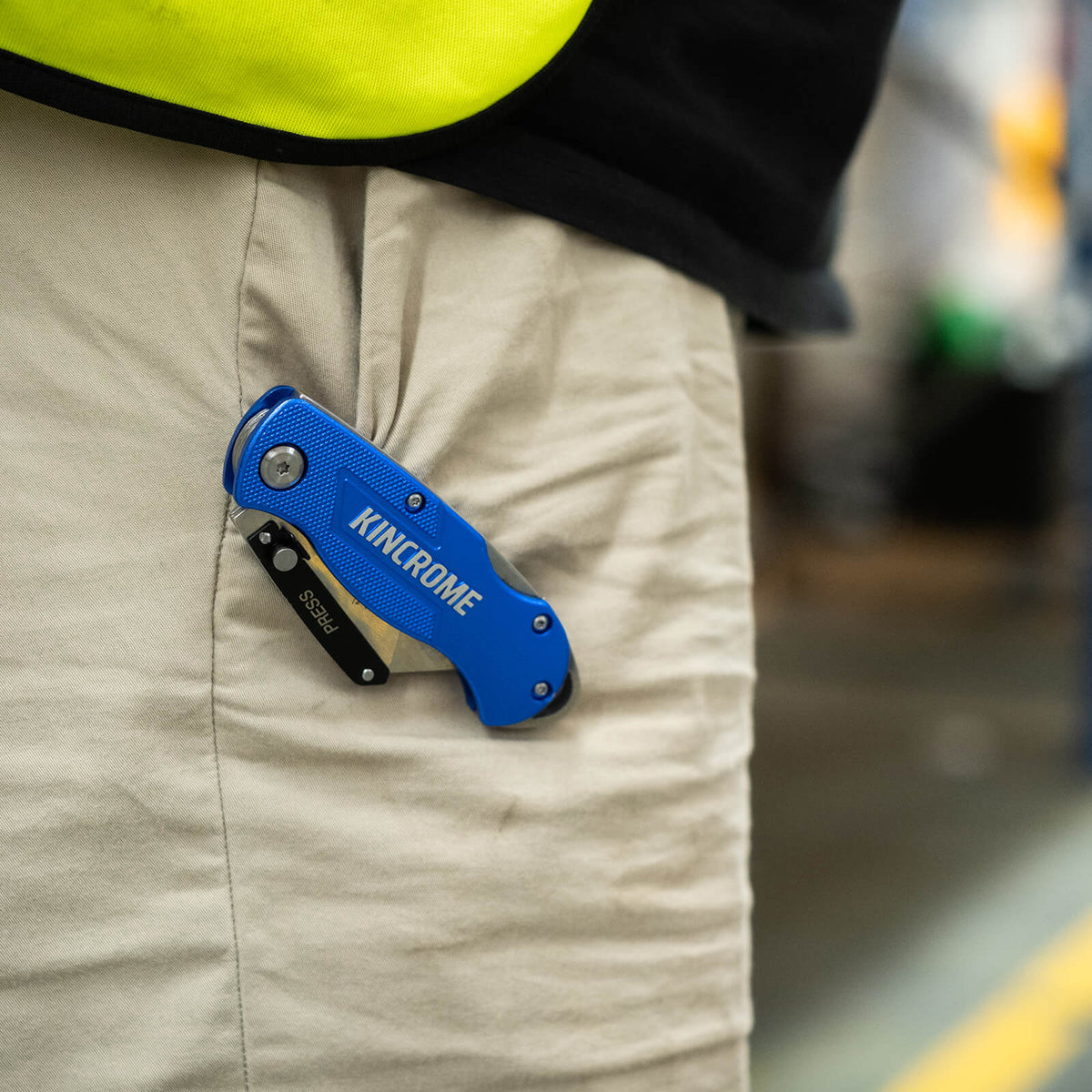 This is an image of a blue Kincrome folding utility knife clipped to beige pants, featured by Kennedys Welding Supplies in Derwent Park TAS, offering tool shop, welding specialists, and power tool repairs