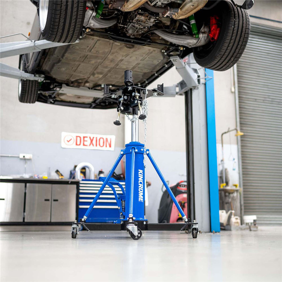 This is an image of a Kincrome blue transmission jack lifting a car in a workshop, Kennedys Welding Supplies, Derwent Park TAS