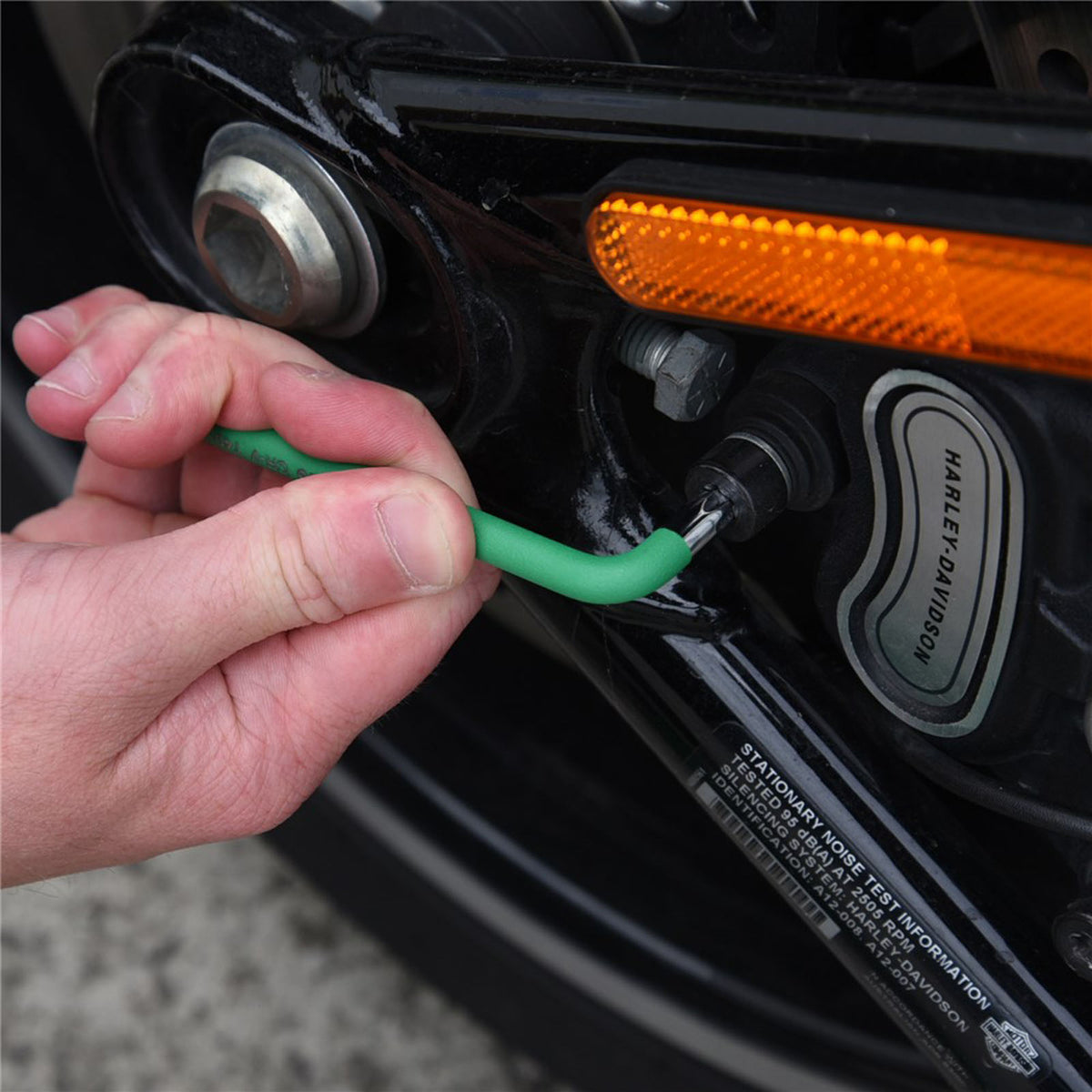 This is an image of hand using a green hex key wrench on a black Harley-Davidson motorcycle part with an orange reflector, showcasing precision tool use at Kennedys Welding Supplies, Derwent Park TAS, experts in Tool Shop, Power Tool Repairs, and Welding Specialists.