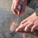 This is an image of hands using a metal scribe and ruler on steel plate, showcasing precise marking by Kennedys Welding Supplies in Derwent Park TAS offering tool shop and welding specialists