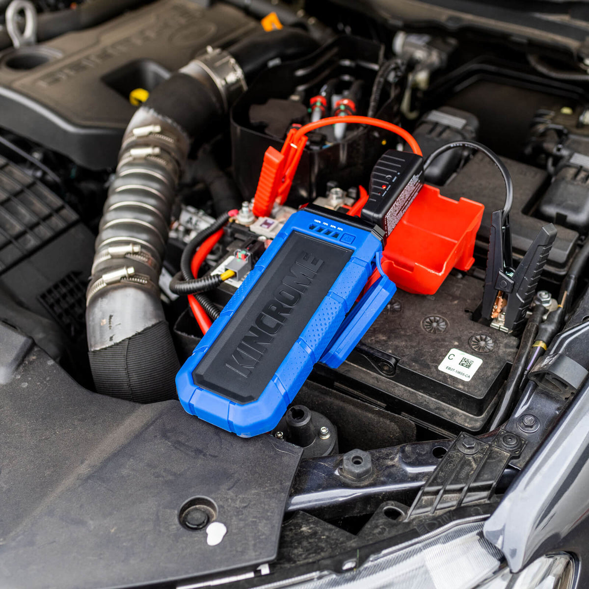 This is an image of a Kincrome blue portable battery charger connected to a car battery under the hood, offered by Kennedys Welding Supplies in Derwent Park, TAS, providing tool shop and power tool repairs services.