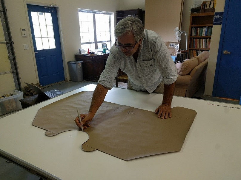 This is an image of a man tracing a large brown paper pattern on a white table, representing precision work related to Kennedys Welding Supplies services in Derwent Park, TAS