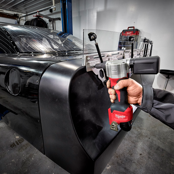 This is an image of a hand holding a red Milwaukee power tool working on a black vehicle part in a workshop at Kennedys Welding Supplies, Derwent Park TAS, welding specialists and tool shop