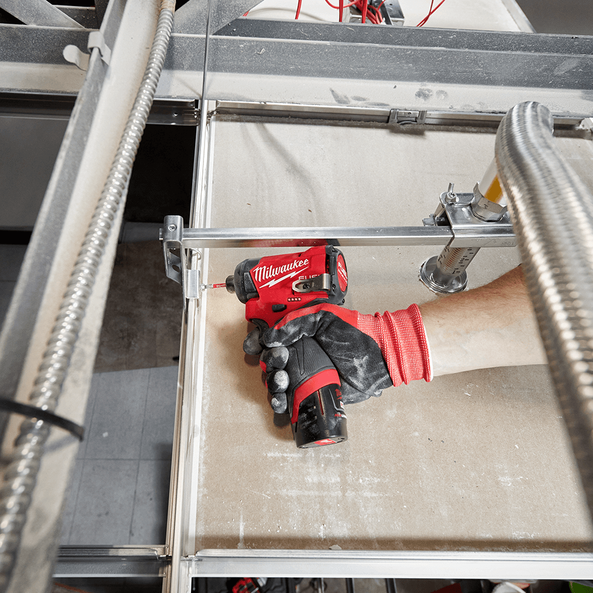 This is an image of a hand in a red and black glove holding a red Milwaukee power tool on a workbench, showcasing tools from Kennedys Welding Supplies in Derwent Park, TAS, offering Tool Shop, Welding Specialists, and Power Tool Repairs