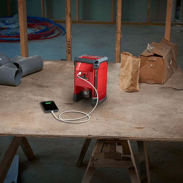 This is an image of a red laser level charging a smartphone on a construction site table, representing Kennedys Welding Supplies in Derwent Park TAS, offering tool shop and laser cutting services
