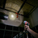 This is an image of a hand holding a Milwaukee spotlight inside an industrial setting, showcasing tools from Kennedys Welding Supplies in Derwent Park, TAS, offering welding specialists and power tool repairs.