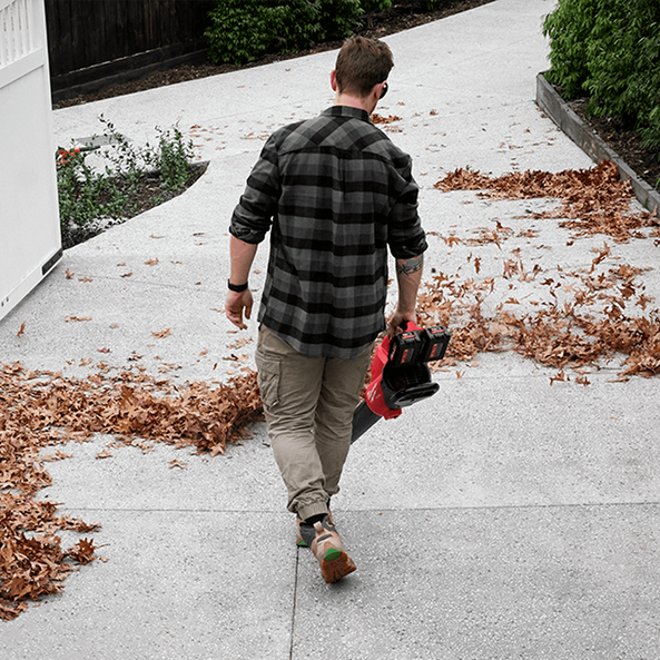 This is an image of a man using a red leaf blower outdoors, showcasing tools available at Kennedys Welding Supplies in Derwent Park, TAS