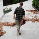 This is an image of a man using a red leaf blower outdoors, showcasing tools available at Kennedys Welding Supplies in Derwent Park, TAS