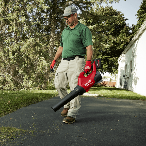 This is an image of a man using a red Milwaukee blower outdoors near a house, showcasing power tools from Kennedys Welding Supplies in Derwent Park, Tasmania, offering welding specialists, tool shop, and power tool repairs.