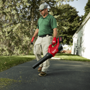 This is an image of a man using a red Milwaukee blower outdoors near a house, showcasing power tools from Kennedys Welding Supplies in Derwent Park, Tasmania, offering welding specialists, tool shop, and power tool repairs.