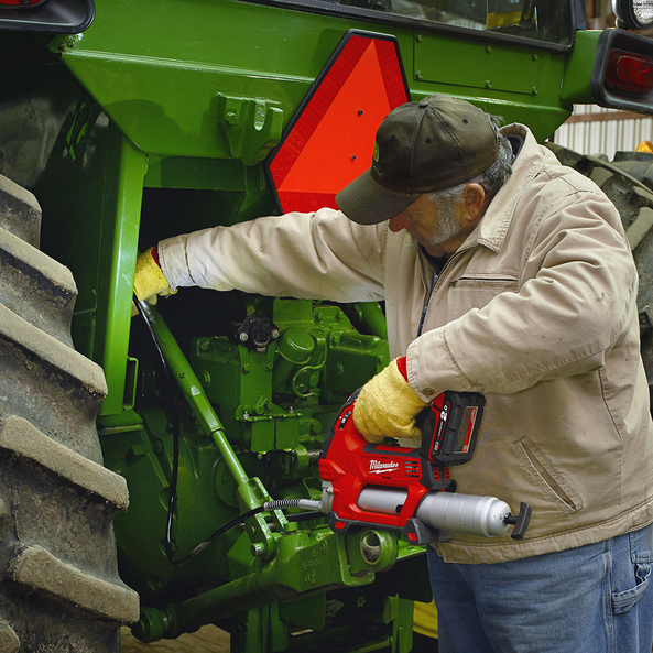 This is an image of a man using a Milwaukee power tool to repair a green tractor at Kennedys Welding Supplies in Derwent Park TAS, offering tool shop and power tool repairs
