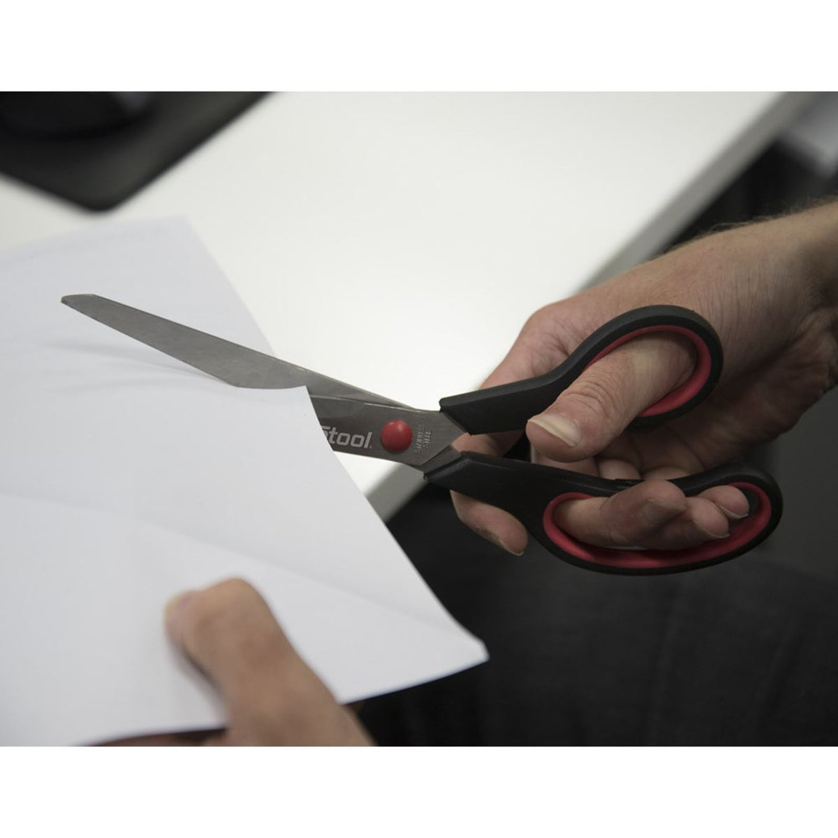 This is an image of a person cutting white paper with black and red scissors, promoting Kennedys Welding Supplies in Derwent Park TAS offering tool shop and power tool repairs.